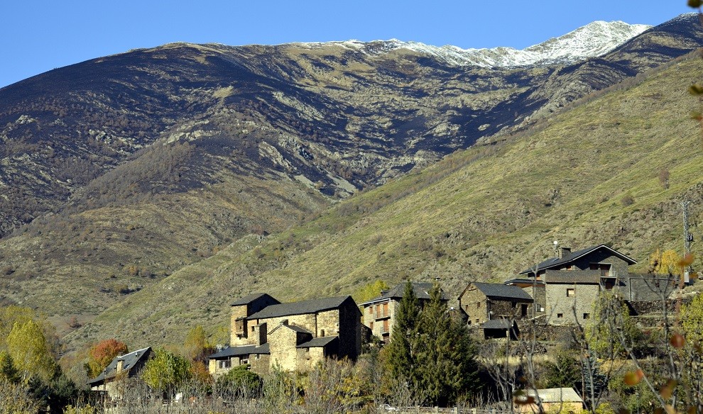 Primer pla del poble de Cerbi amb la muntanya al fons cremada