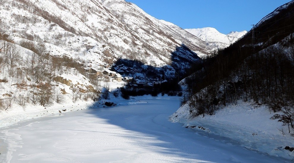 El pantà de Tavascan, congelat, amb el poble nevat al fons