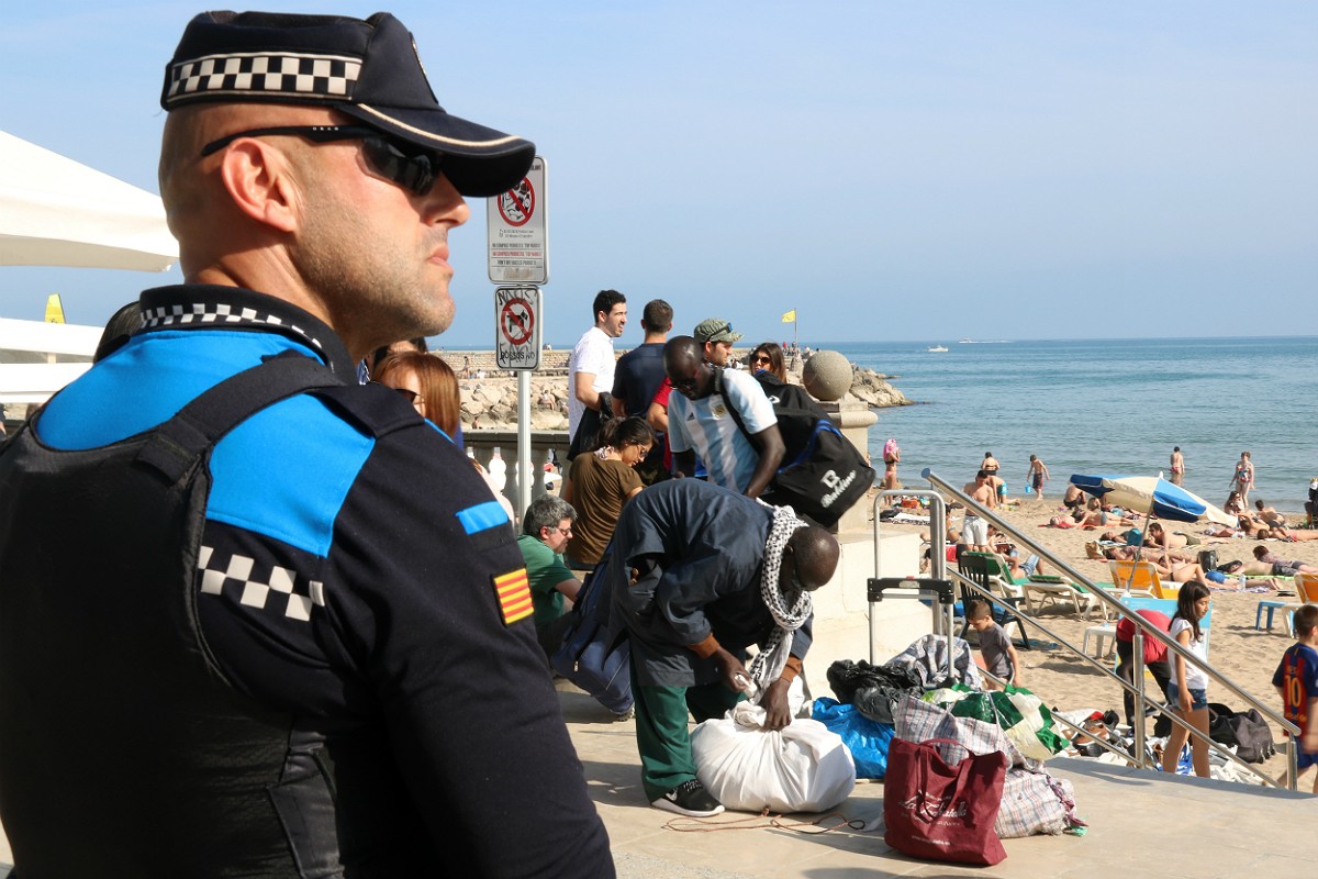 Un agent de la Policia Local de Sitges, amb manters al fons recollint els seus productes