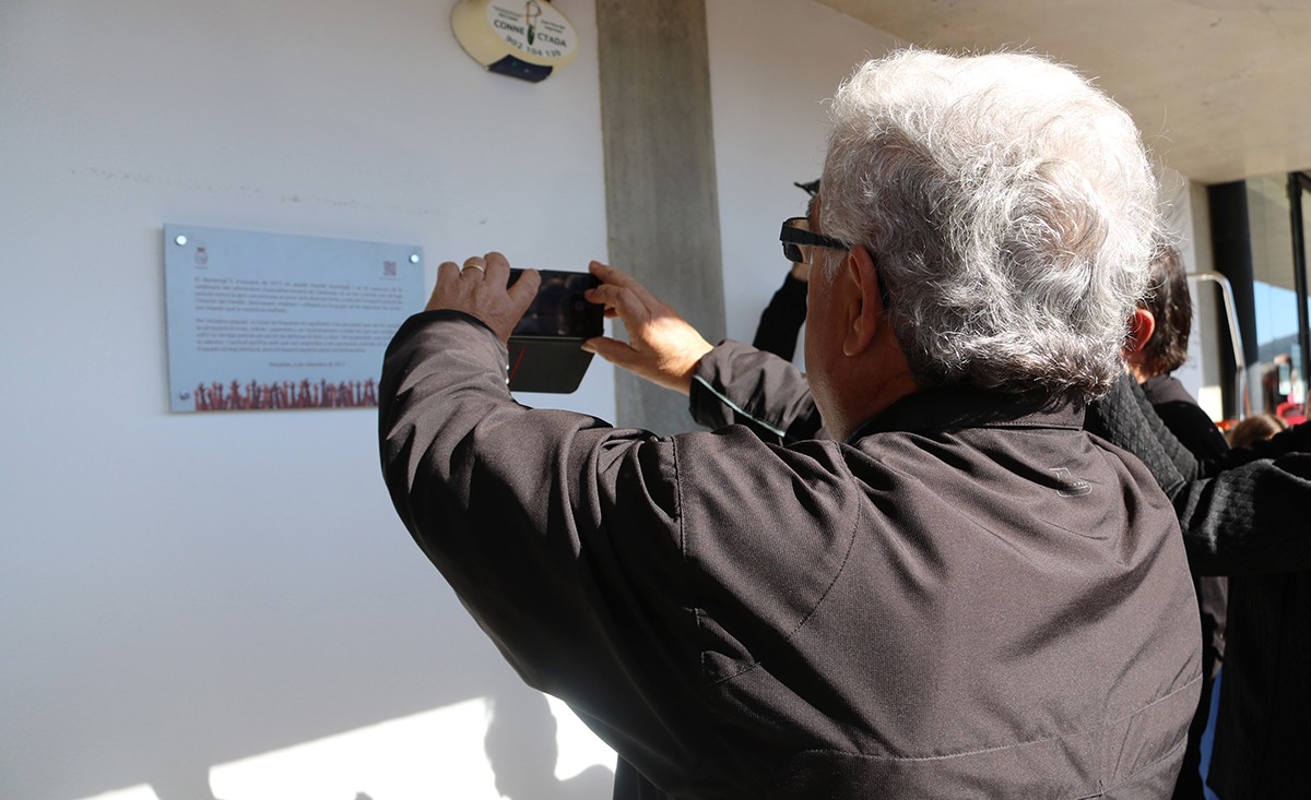 Pla mig d'un home, d'esquenes, fent una fotografia a la placa commemorativa de l'1-O a Roquetes.