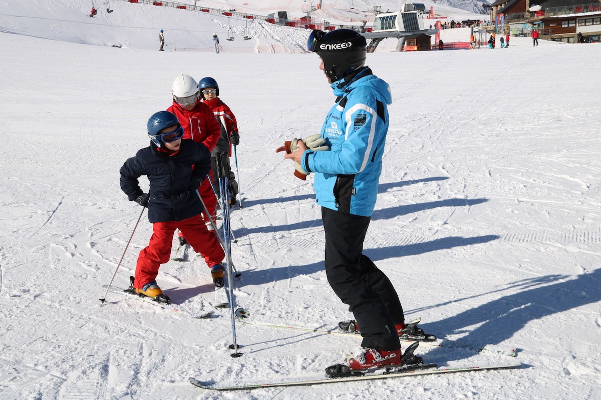 Un monitor d'esquí fa una classe d'esquí alpí a tres escolars