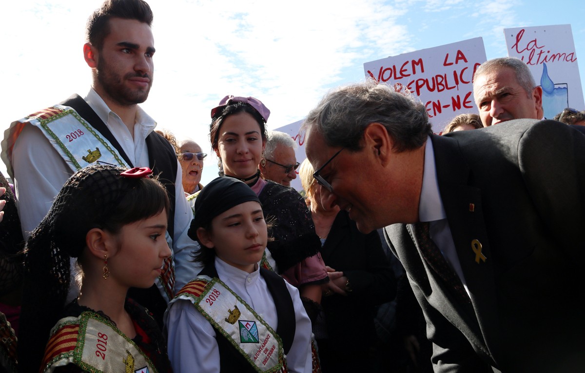 El president de la Generalitat, Quim Torra, rebut per dues xiquetes en la seua arribada al Centre Fluvial del Delta i amb pancartes al fons de protesta. 