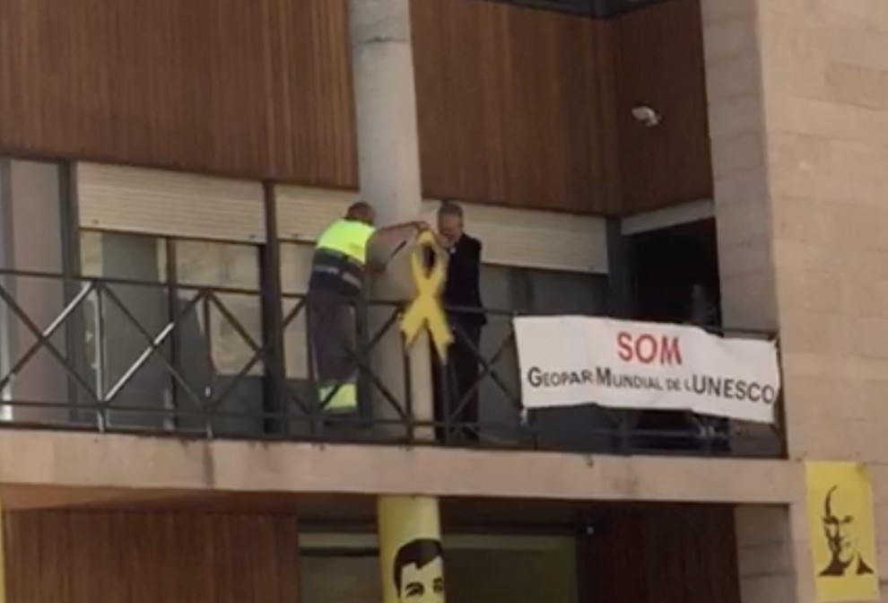 Ubach i un treballador municipal retirant el llaç groc del balcó