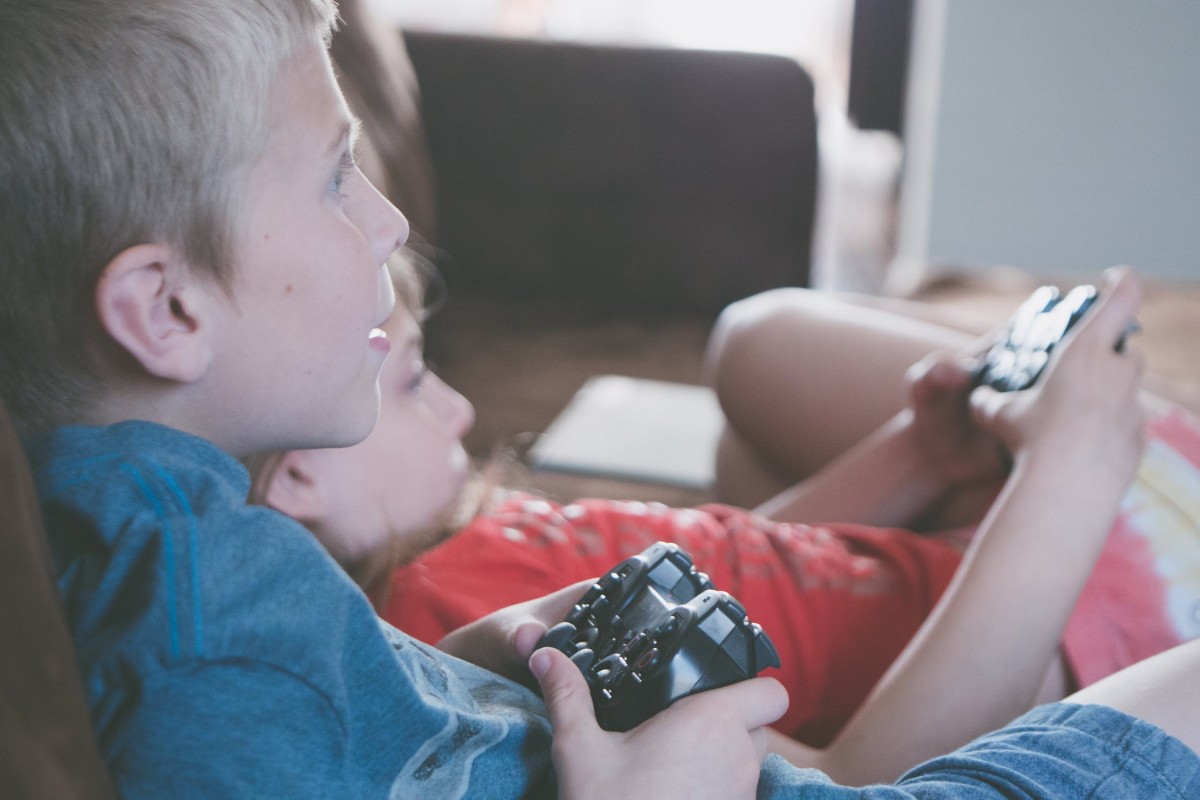 Dos nens, jugant a videojocs des del sofà de casa.