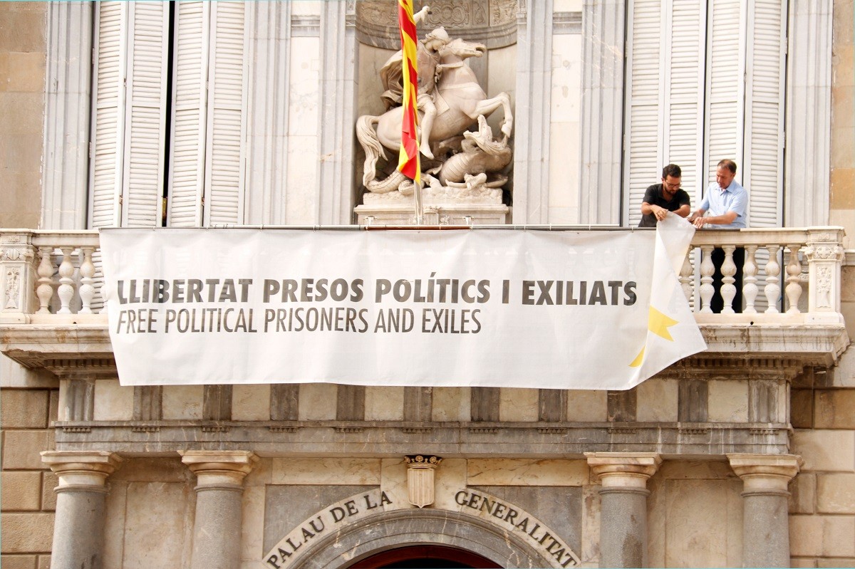 Dos treballadors de la Generalitat despengen del balcó de Palau la pancarta que demana la llibertat dels presos