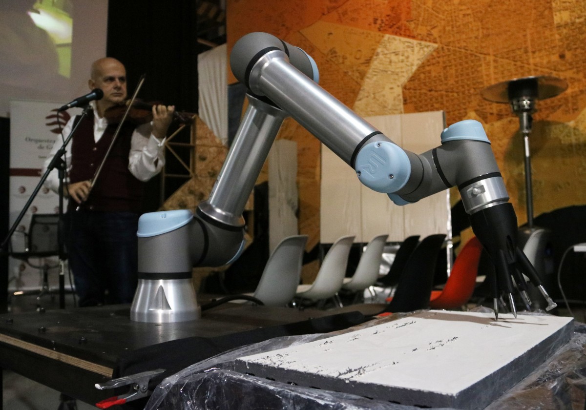 Un robot rebent impulsos d'un instrument pintant sobre una ceràmica en el marc del projecte 'Els elements & Robot Orchestra' amb la Orquestra de Cambra de Granollers