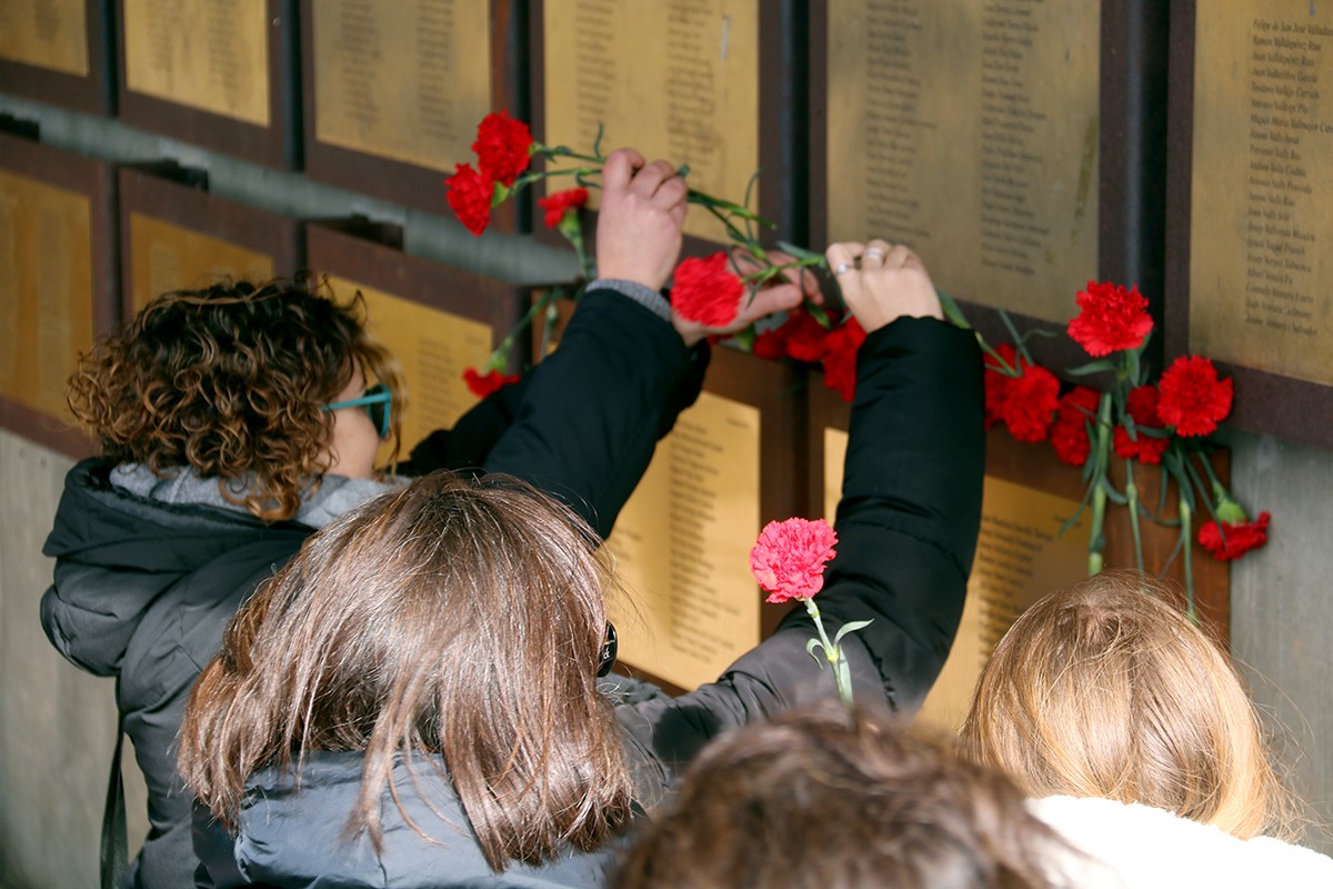 Alguns familiars dipositant clavells rojos sota les plaques que recorden les víctimes de la Guerra Civil al memorial de les Camposines