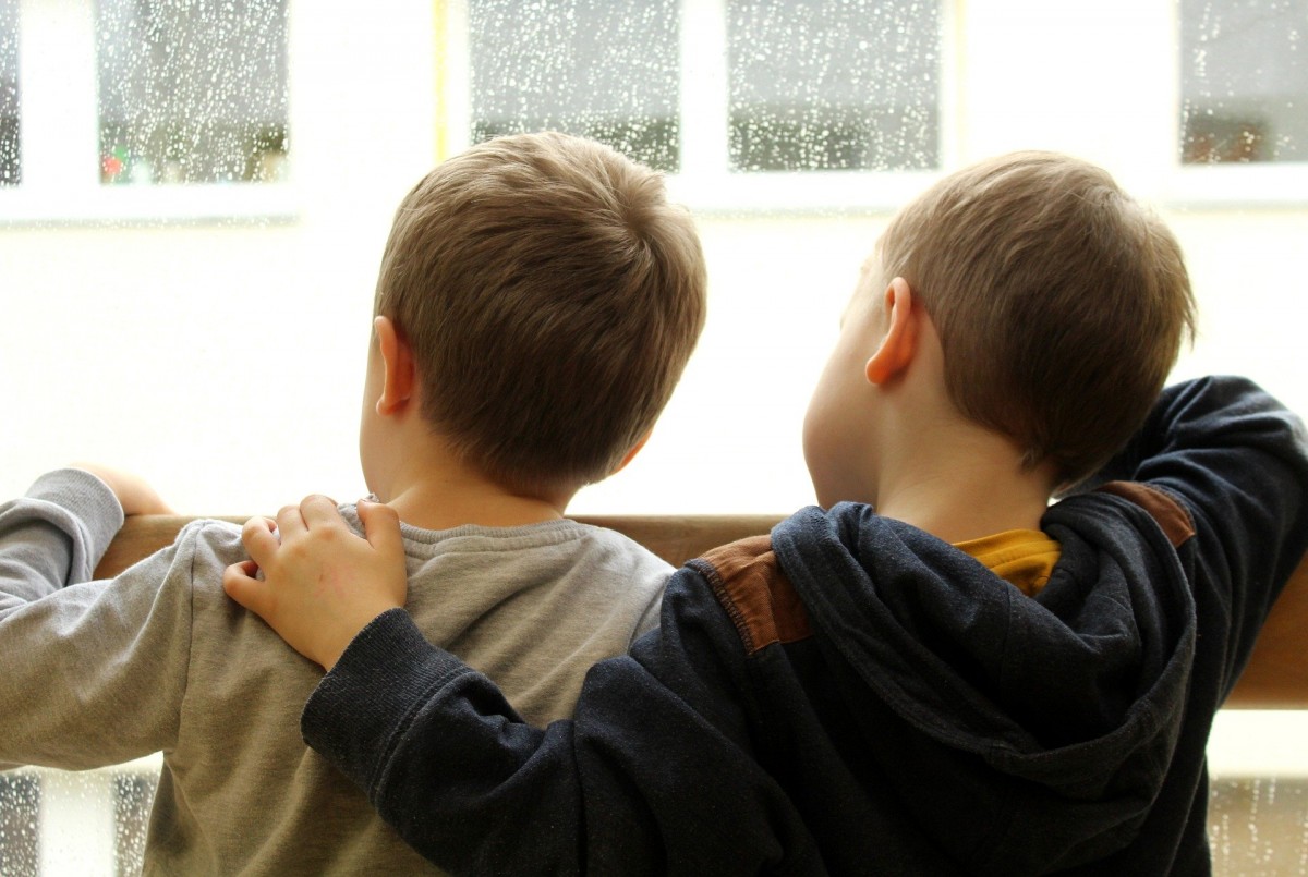 Dos nens mirant per la finestra des de casa.