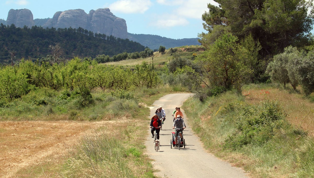 Un grup de visitants dirigint-se amb bicicleta la via verda, a Horta de Sant Joan, amb les roques de Benet al fons.