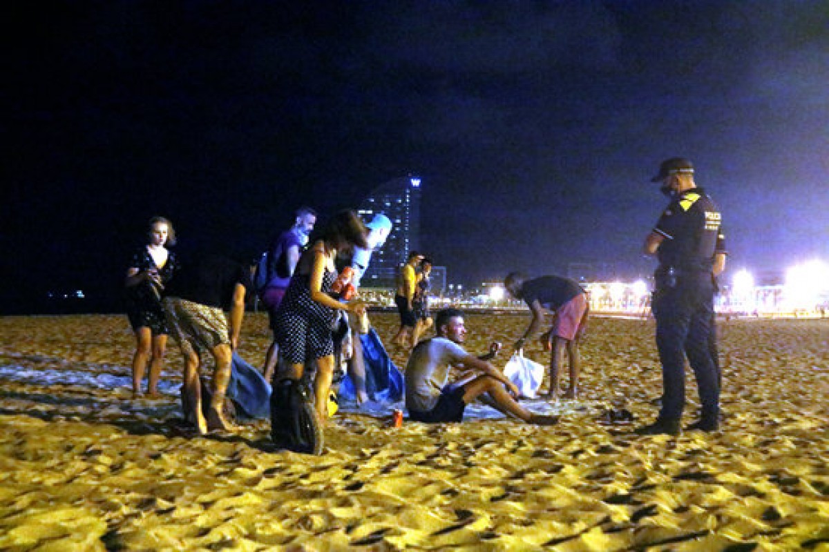 Un grup de persones que feia el botellot a la platja de la Barceloneta de Barcelona s'aixequen davant la presència d'una línia d'agents de la Guàrdia Urbana