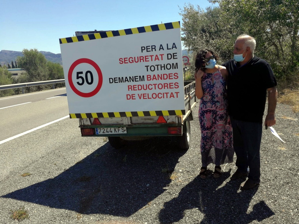 Dos dels veïns de la nova plataforma d'Ascó al costat del cartell reivindicatiu per demanar millores en seguretat viaria a la C-12 que col·loquen cada dia.