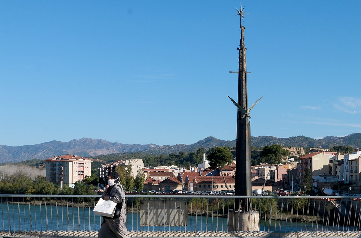 Una vianant camina pel pont de l'Estat de Tortosa amb el monument franquista al fons