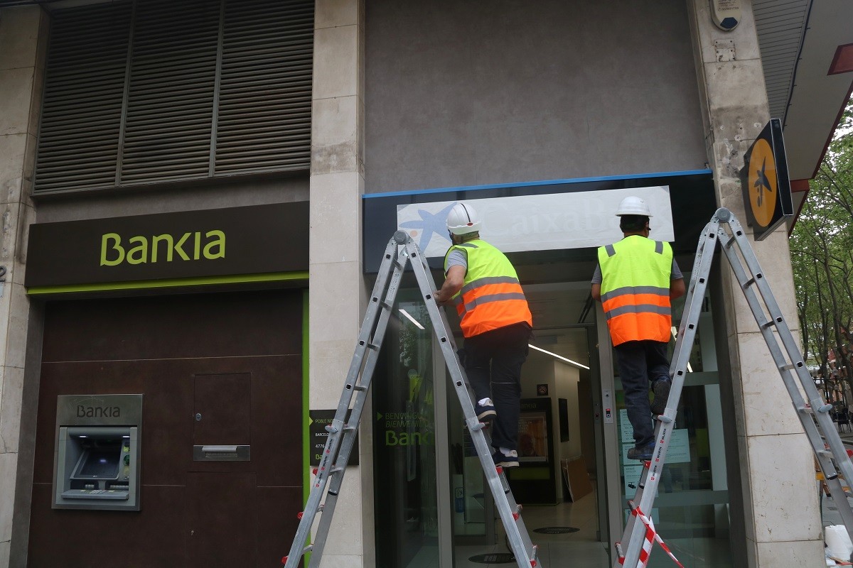 Dos operaris canviant la marca de Bankia a CaixaBank a l'oficina