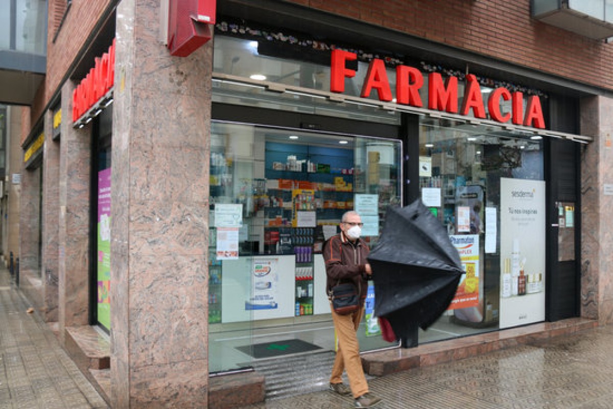 Un home obre un paraigües a la sortida d'una farmàcia