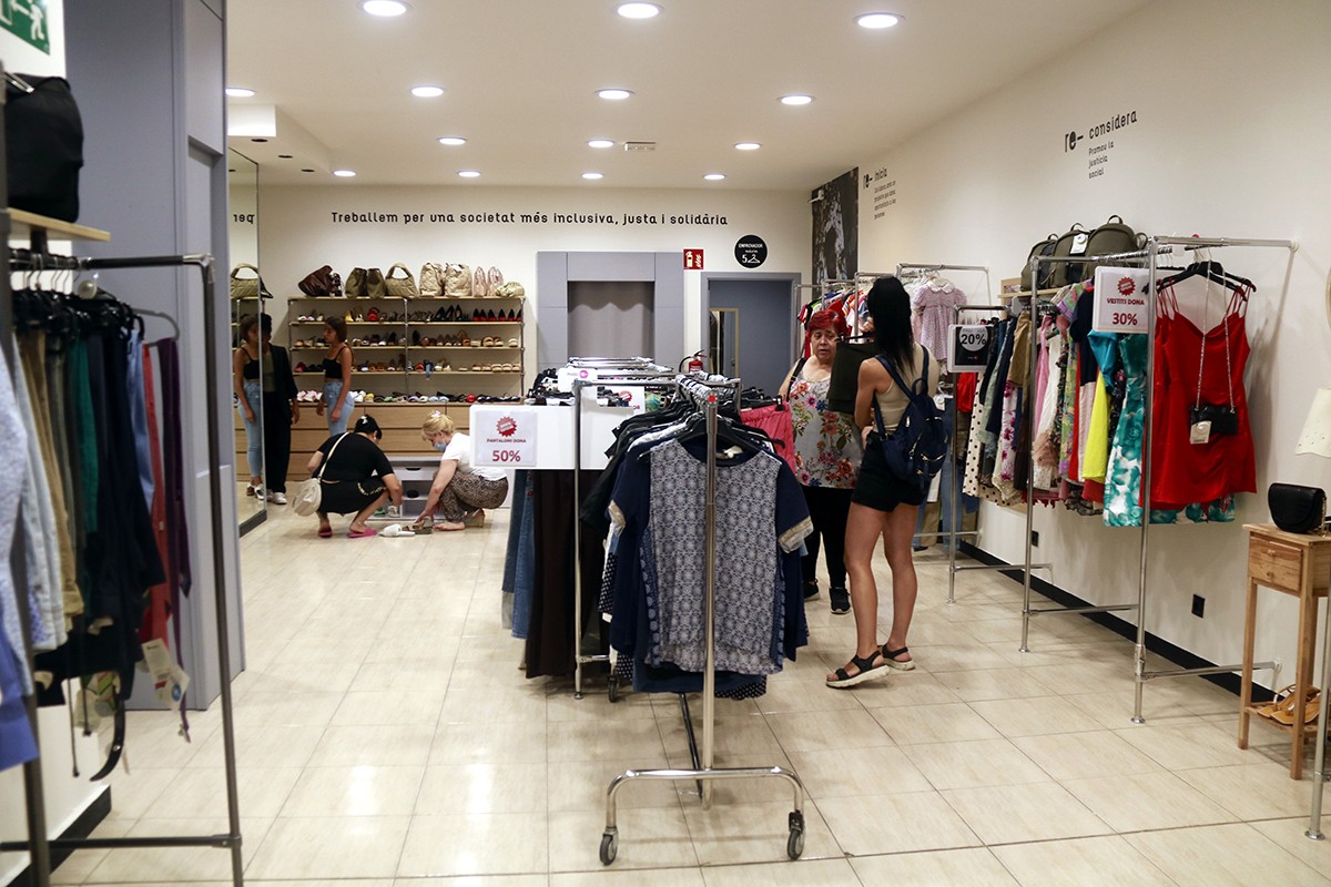 Gent mirant roba i calçat a una de les botigues de moda de segona mà de Càritas a Lleida.