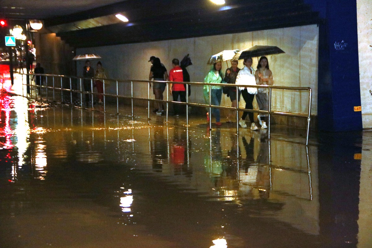 Un grup de persones passa per un pont del barri del Serrallo inundat per la pluja