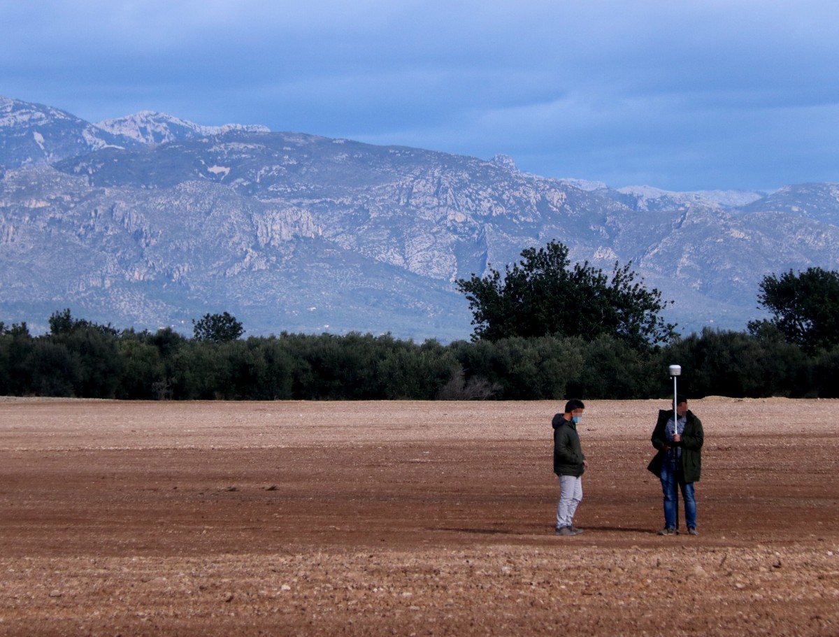 Pla general dels terrenys on es projecta la planta de compostatge a Santa Bàrbara amb dos persones prenent mesures del terreny. Imatge del 12 de febrer de 2021. 