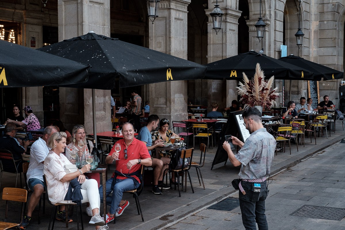 Un cambrer fotografia un grup de turistes en una terrassa de la plaça Reial.
