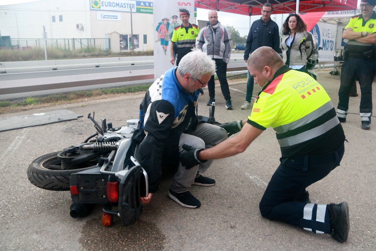 Un Mosso d'Esquadra ensenya a aixecar una motocicleta de forma segura a un usuari de la jornada de mobilitat segura a Roquetes, este dissabte 