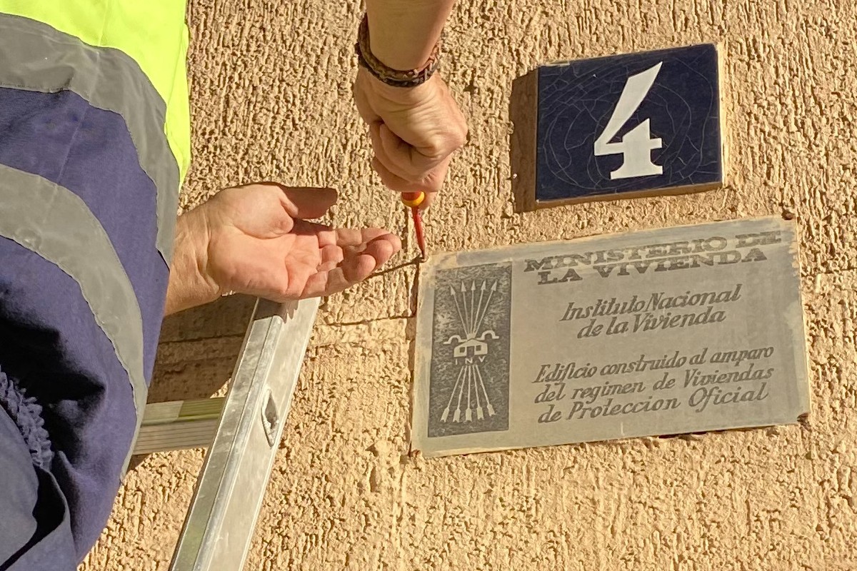 Un operari, tot retirant una placa franquista de la façana d'un bloc de pisos del Morell