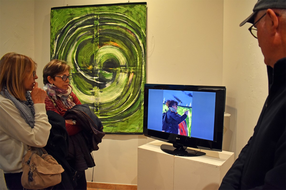 Persones assistents a la inauguració de l'exposició sobre Mabel Nieto miren un vídeo de l'artista surienca