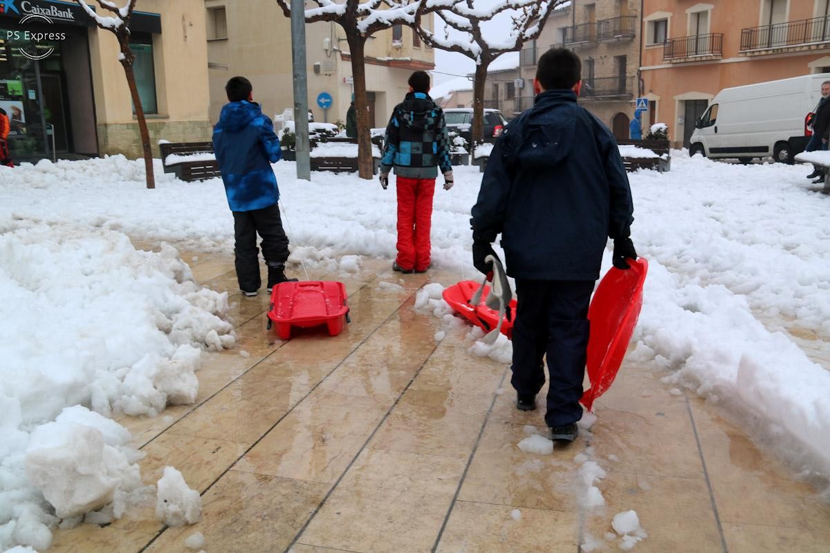 Trens nens amb trineus creuen la plaça plena de neu a Horta de Sant Joan  