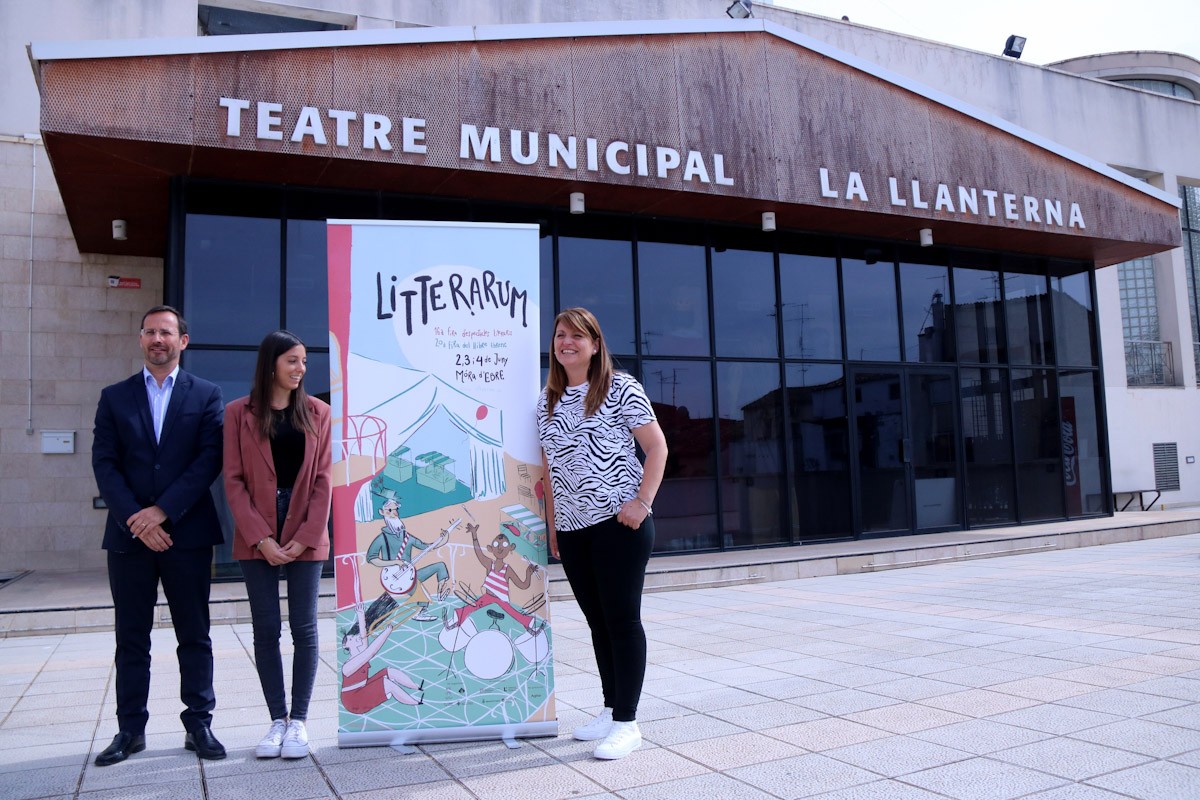 L'alcalde de Móra d'Ebre, Rubén Biarnés; la directora de Litterarum, Gemma Sastre; i la regidora de Cultura, Montse Pineda, amb el cartell de la setzena edició de Litterarum davant la façana del teatre La Llanterna  