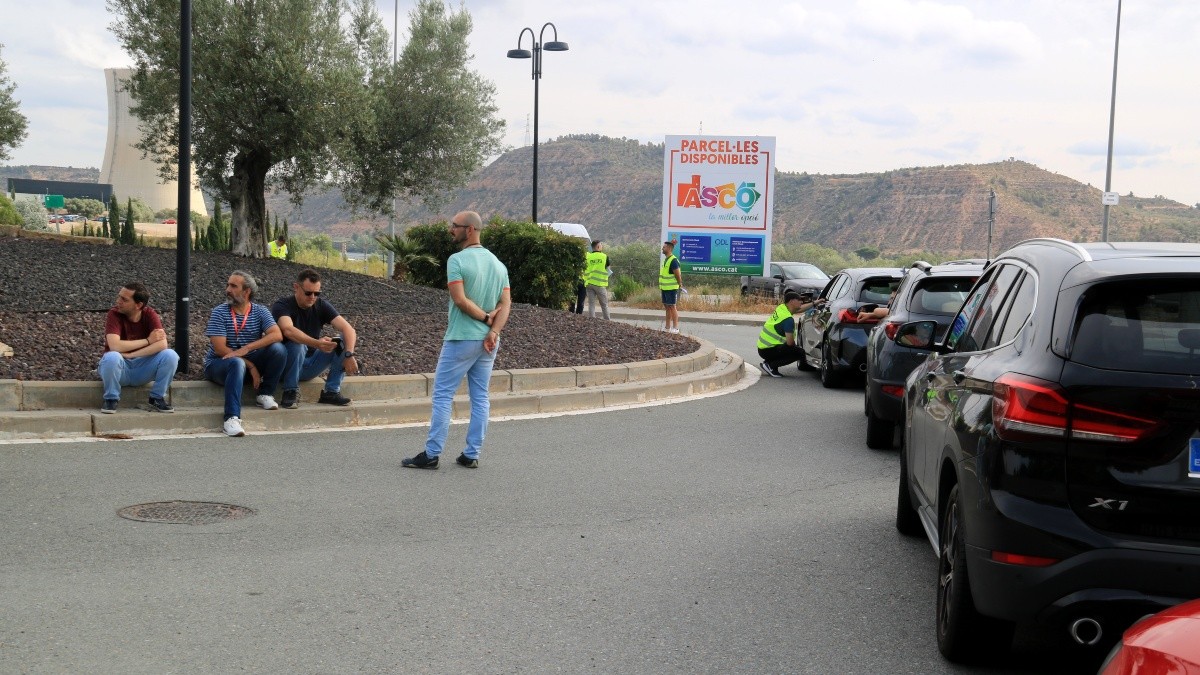 Vehicles aturats i treballadors asseguts esperant a la vorera en la rotonda d'accés a la nuclear d'Ascó.