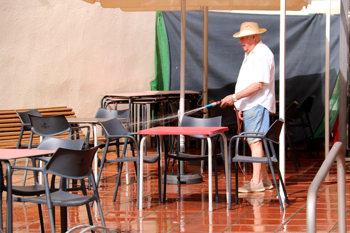 Un home refresca amb una mànega d'aigua la terrassa del local on ens avis van a passar la tarda a Vinebre  